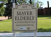 Thumbnail 10 of 18 - A sign for Mayer Elderly Apartments stands on a sidewalk.