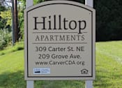 Thumbnail 2 of 18 - A sign for Hilltop Apartments is displayed in front of a green lawn.