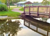 Thumbnail 15 of 54 - a bridge over a body of water with a picnic shelter in the background