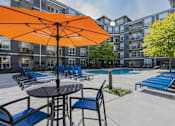 Thumbnail 25 of 29 - A large orange umbrella is in the middle of a poolside table and chairs.