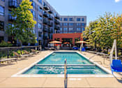 Thumbnail 29 of 29 - A swimming pool surrounded by chairs and trees in front of a building.