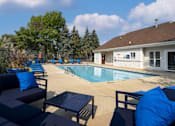 Thumbnail 4 of 19 - A pool area with blue cushions and a white building in the background.