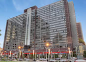 Thumbnail 12 of 13 - A large red and grey building with a parking lot in front.