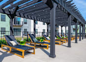 Thumbnail 12 of 13 - A row of sun loungers are arranged under a wooden pergola.