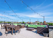Thumbnail 9 of 13 - A rooftop patio with wooden flooring, tables and chairs, and string lights.