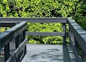 Thumbnail 11 of 27 - A wooden bridge with a metal railing leads through a lush green forest.