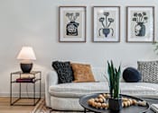 Thumbnail 36 of 127 - A living room with a white couch, a lamp, and three framed pictures on the wall.