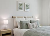 Thumbnail 56 of 116 - A bed with a white comforter and a lamp on a nightstand. at Park South Apartments, Austin, Texas