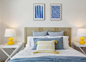 Thumbnail 65 of 116 - A bed with a blue comforter and yellow pillows is flanked by two white tables with yellow lamps. at Park South Apartments, Texas, 78748