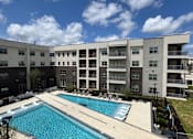 Thumbnail 1 of 21 - A large swimming pool in front of apartment buildings.