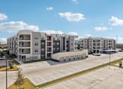 Thumbnail 97 of 103 - Modern apartment building with parking area at Cantarra Apartments, Manor, TX