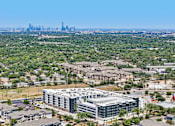 Thumbnail 62 of 127 - A large building complex is in the foreground with a city skyline in the background.