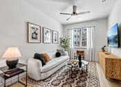 Thumbnail 30 of 127 - A living room with a white couch, a coffee table, a ceiling fan, and a flat screen TV mounted on the wall.