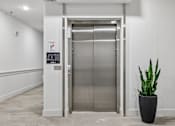 Thumbnail 69 of 127 - A silver elevator with a sign on the wall and a plant in a pot.