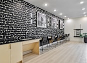 Thumbnail 90 of 127 - A black and white photo of a room with a brick wall and a row of chairs.