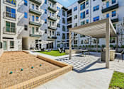 Thumbnail 106 of 127 - A modern apartment complex with a sandy courtyard and a wooden pergola.