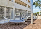 Thumbnail 108 of 127 - A hammock is strung between two poles in front of a concrete building.