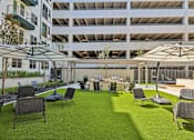 Thumbnail 109 of 127 - A patio area with chairs and tables is surrounded by a parking garage.