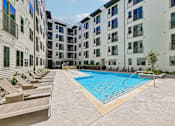 Thumbnail 115 of 127 - A swimming pool surrounded by sun loungers in front of apartment buildings.