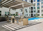 Thumbnail 120 of 127 - A pool area with a grill and a building in the background.