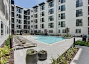 Thumbnail 1 of 46 - A pool surrounded by lounge chairs and planters in front of apartment buildings.