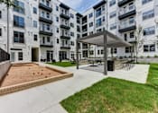Thumbnail 23 of 46 - A playground area with a sandbox and a pavilion is located in front of a white apartment building.