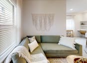 Thumbnail 15 of 21 - A living room with a green couch and a white wall hanging.