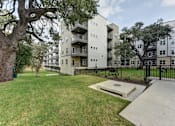 Thumbnail 83 of 140 - Courtyard green space with pathway and mature oak trees at Matador Apartments, Austin, TX