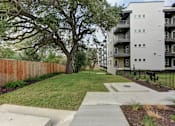 Thumbnail 86 of 140 - Outdoor green space with mature trees and wooden fence at Matador Apartments, Austin