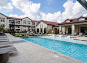 Thumbnail 13 of 55 - A pool area with sun loungers and a building in the background.