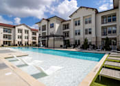 Thumbnail 16 of 55 - A swimming pool surrounded by lounge chairs and buildings in the background.