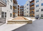 Thumbnail 15 of 51 - A courtyard surrounded by apartment buildings with a stone wall and a bench.