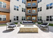 Thumbnail 16 of 51 - A modern outdoor seating area with a stone fireplace in front of a multi-story apartment building.