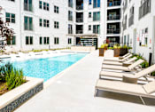 Thumbnail 31 of 46 - A pool surrounded by chairs and plants in front of a white building.