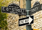 Thumbnail 44 of 46 - A street sign pole with signs for E 6th Street, Trinity Street, and a one way sign.