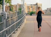 Thumbnail 43 of 46 - A woman is running on a sidewalk next to a metal fence.