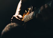Thumbnail 41 of 46 - A person playing a guitar in a dimly lit room.