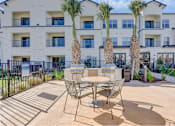 Thumbnail 25 of 80 - A patio with a table and chairs is surrounded by palm trees.