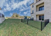 Thumbnail 31 of 80 - A black metal fence surrounds a grassy yard in front of a two-story building.