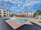 Thumbnail 55 of 80 - A swimming pool in front of a building with a blue sky and clouds in the background.