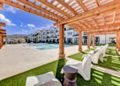 Thumbnail 57 of 80 - A wooden pergola over a patio with white chairs and a pool in the background.