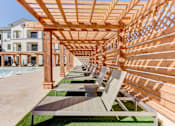 Thumbnail 59 of 80 - A wooden pergola with benches is in the foreground of a building.