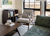 Thumbnail 5 of 15 - A living room with a chair, a table, a book and a painting.