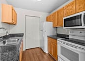 Thumbnail 33 of 40 - A kitchen with a white refrigerator, black countertops, and wooden cabinets.