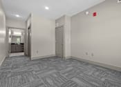 Thumbnail 26 of 39 - A hallway with a grey carpet and a red fire alarm on the wall.