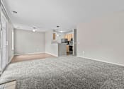 Thumbnail 26 of 40 - A spacious room with a grey carpet and a kitchen area in the background.