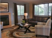 Thumbnail 4 of 14 - The leasing office at Brighton Cove. There is a leather couch under a big picture window. An end table with a lamp is to the left of the couch. A stripped chair is to the right of the couch. A glass and wooden coffee table is in front of the couch. Under it is a brown, tan, and blue pattered rug.
