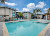 Thumbnail 4 of 57 - A large swimming pool in front of a building with a blue sky and clouds in the background.