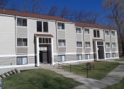 Thumbnail 7 of 16 - Exterior of building from the parking lot.  Sidwalk runs horizontal to building and there are 2 entrance doors.  Each door has white pillars on each side.  Building has beige siding with white trim.  Grass is green.