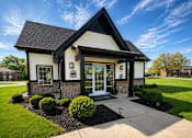 Thumbnail 1 of 18 - A small white building with a black roof and a glass door.